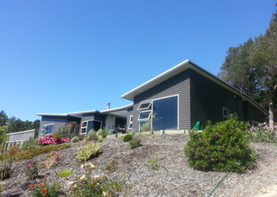 New build house with dark gray weather board cladding. Situated on a bank that is fully landscaped by the team at Quadrille Construction