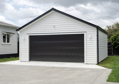 Typical double detached white garage with black tilt up retractable raised panel metal door and gable metal roof